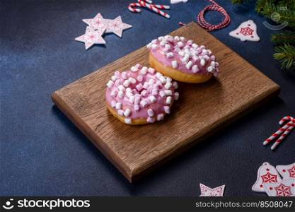 Pink glazed doughnut and marshmallow with Christmas decorations on a wooden cutting board against a dark concrete background. Pink glazed doughnut and marshmallow with Christmas decorations on a wooden cutting board