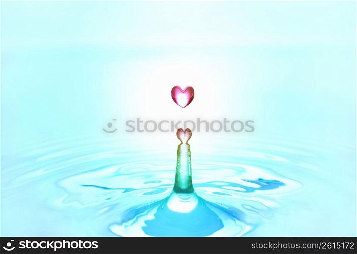 Pink heart shaped water droplets falling into blue water
