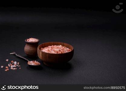 Pink himalayan salt in a wooden bowl on a dark concrete background. Seasonings and additives in the kitchen
