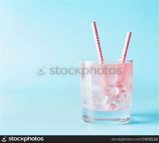 Pink iced refreshment drink in glass with paper drink straw on blue background. Copy space. Summer pastel pink cocktail.