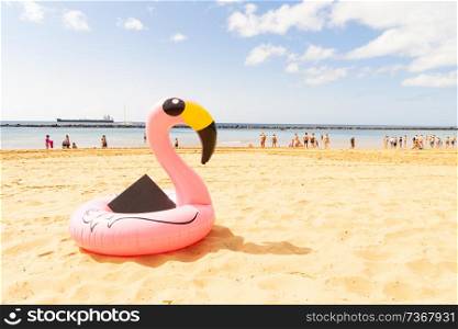 Pink inflatable flamingo in sand on summer beach. Pink flamingo on beach