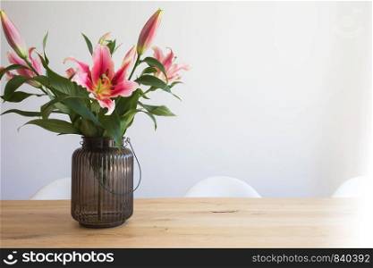 pink lily flowers in a vase on a wooden table in the interior against a white wall in modern room beauty. pink lily flowers in a vase on a wooden table in the interior against a white wall in modern room