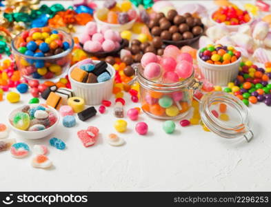 Pink lollipop candies in jar with various milk chocolate and jelly gums candies on white with liquorice allsorts and strawberry bonbons