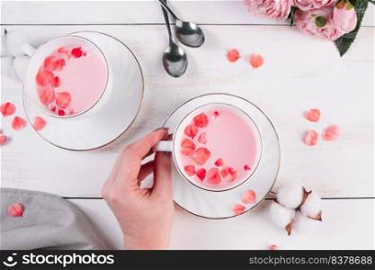 Pink matcha with rose petals on a white background. Female hand holds a cup with trending vegan tea. Relaxing drink in the sleepy time.. Pink matcha with rose petals on white background. Female hand holds a cup with trending vegan tea. Relaxing drink in the sleepy time.