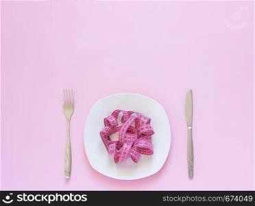 Pink measuring tape lying on plate in the form of spaghetti, knife and fork on pink background. Diet or anorexia concept. Top view Copy space. Pink measuring tape lying on plate in the form of spaghetti, knife and fork on pink background