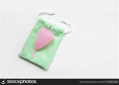 Pink menstrual cup on green small bag on white background. Concept zero waste, savings, minimalism, these days. Feminine hygiene product, flat lay, copy space. Horizontal.