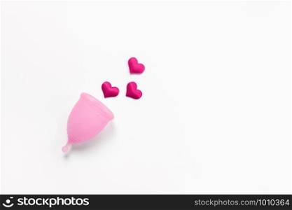 Pink menstrual cup on white background with crimson hearts. Concept zero waste, savings, minimalism, these days. Feminine hygiene product, flat lay, copy space. Horizontal.