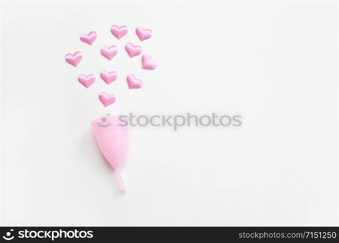 Pink menstrual cup on white background with small hearts. Concept zero waste, savings, environmental conservation, sustainable lifestyle. Feminine hygiene product, flatlay, copy space. Horizontal.