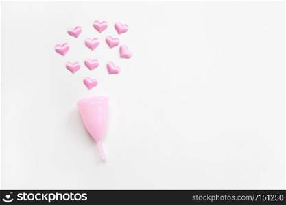 Pink menstrual cup on white background with small hearts. Concept zero waste, savings, environmental conservation, sustainable lifestyle. Feminine hygiene product, flatlay, copy space. Horizontal.