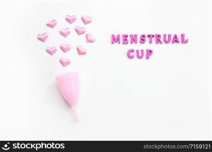 Pink menstrual cup on white background with small hearts and inscription. Concept zero waste, savings, environmental conservation, sustainable lifestyle. Feminine hygiene product, flatlay. Horizontal.