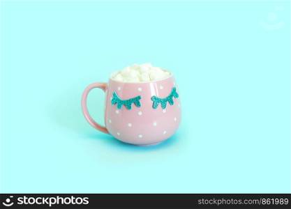 Pink mug with white polka dots with blue closed eyes with coffee and marshmallows. Shiny eyelashes. Blue background.