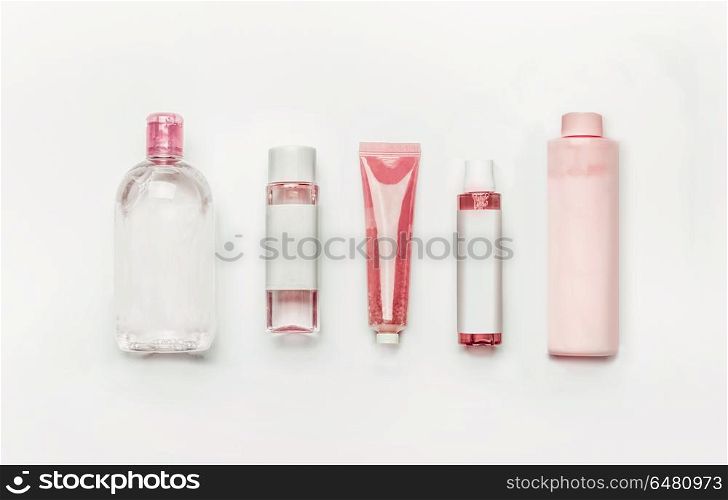 Pink natural cosmetic products : gel, lotion, serum, micellar water and toner, bottles and tubes with branding mock up on white desk background , top view, flat lay . Facial skin care and beauty