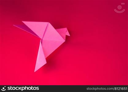 Pink paper dove origami isolated on a blank red background.. Pink paper dove origami isolated on a red background