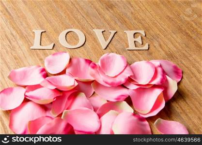 Pink petals with the word love on wooden background