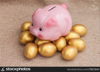 Pink piggy bank climb on heap of golden easter egg on brown sack