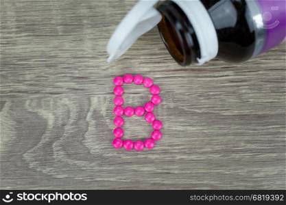 Pink pills forming shape to B alphabet on wood background &#xA;