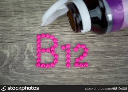 Pink pills forming shape to B12 alphabet on wood background&#xA;