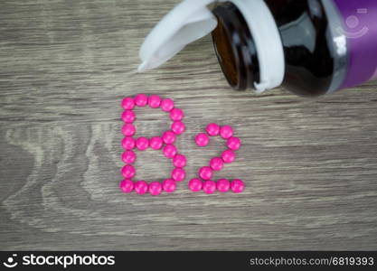 Pink pills forming shape to B2 alphabet on wood background &#xA;