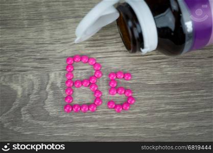 Pink pills forming shape to B5 alphabet on wood background&#xA;