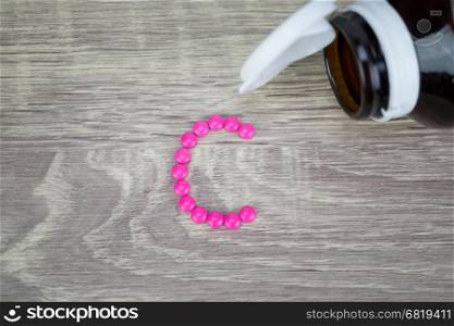 Pink pills forming shape to C alphabet on wood background&#xA;