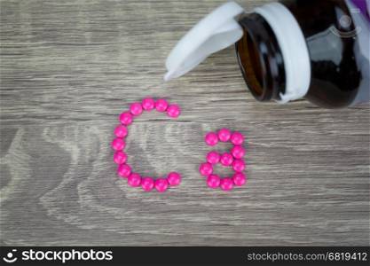 Pink pills forming shape to Ca alphabet on wood background&#xA;