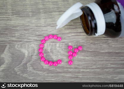 Pink pills forming shape to Cr alphabet on wood background&#xA;