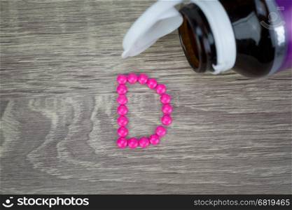 Pink pills forming shape to D alphabet on wood background&#xA;