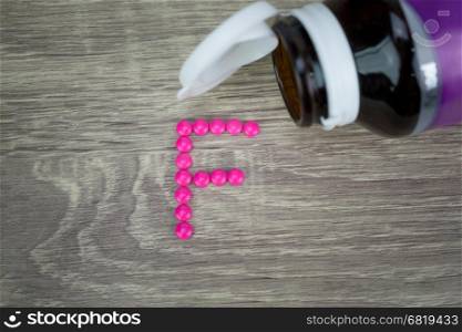 Pink pills forming shape to F alphabet on wood background&#xA;