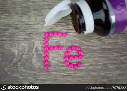 Pink pills forming shape to Fe alphabet on wood background