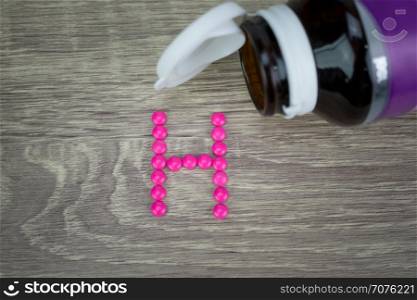 Pink pills forming shape to H alphabet on wood background