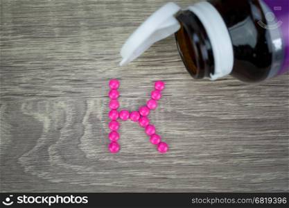 Pink pills forming shape to K alphabet on wood background&#xA;