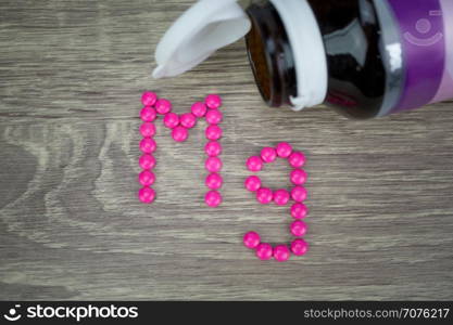 Pink pills forming shape to Mg alphabet on wood background