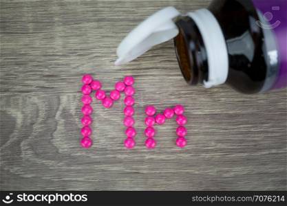 Pink pills forming shape to Mn alphabet on wood background