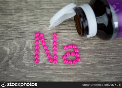 Pink pills forming shape to Na alphabet on wood background