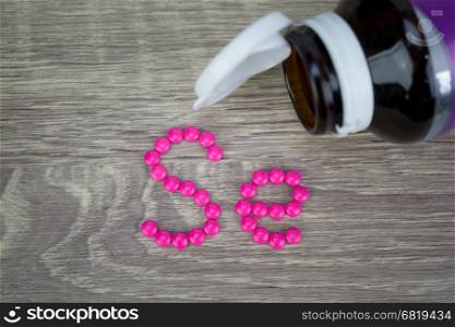 Pink pills forming shape to Se alphabet on wood background&#xA;