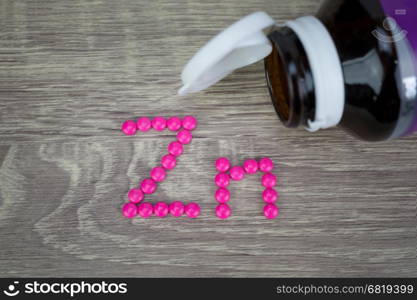 Pink pills forming shape to Zn alphabet on wood background&#xA;