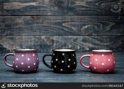 Pink, purple and black ceramic mugs with white dots on blue wooden background