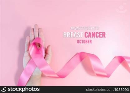 Pink ribbon symbol. Breast Cancer Awareness Month Campaign. Woman hand hold the pink ribbon on pink background