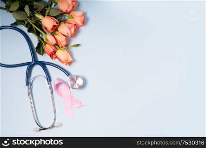 Pink ribbon, symbol of breast cancer awareness with stethoscope and flowers, copy space on blue background. Pink ribbon, symbol of breast cancer awareness