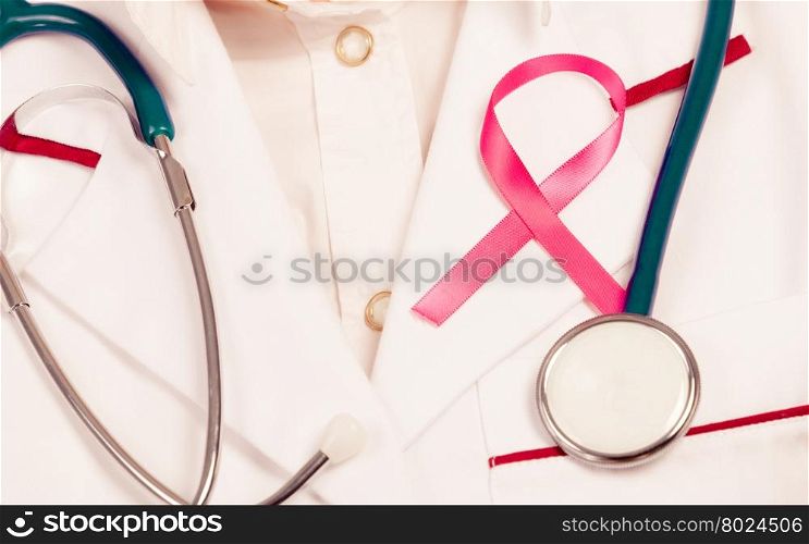 Pink ribbon with stethoscope on medical uniform.. Women fight for health. Breast cancer tumor concept. Pink ribbon and blue stethoscope on white medical apron uniform.
