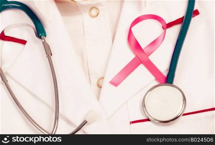 Pink ribbon with stethoscope on medical uniform.. Women fight for health. Breast cancer tumor concept. Pink ribbon and blue stethoscope on white medical apron uniform.