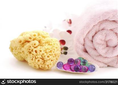 Pink rolled up towel with bath beads and natural sponge on white background
