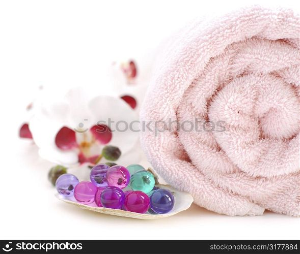 Pink rolled up towel with bath beads on white background