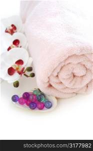 Pink rolled up towel with bath beads on white background
