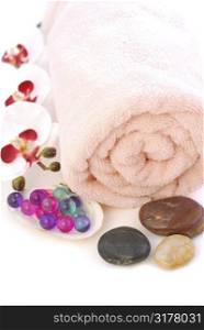Pink rolled up towel with massage stones and bath beads on white background