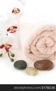 Pink rolled up towel with massage stones on white background