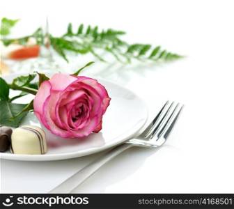 pink rose and chocolate candy on a white plate