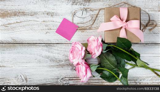 Pink roses and gift box for romantic celebrations on rustic white wood in flat lay view