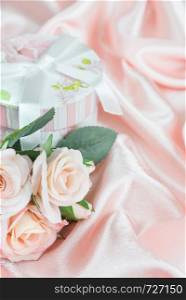 Pink roses and gift box with bow on a background of the silk fabric, vertical image