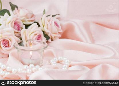 pink roses, burning candle and a pearl necklace on a silk fabric